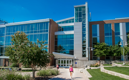 A student in a pink shirt walking in front of the Science building on the Rockville Campus
