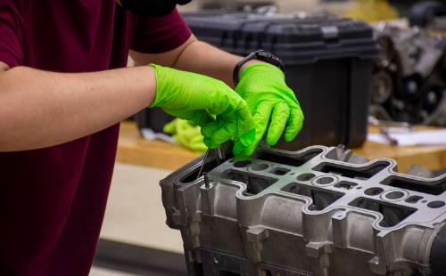 student gloved hands working on auto engine