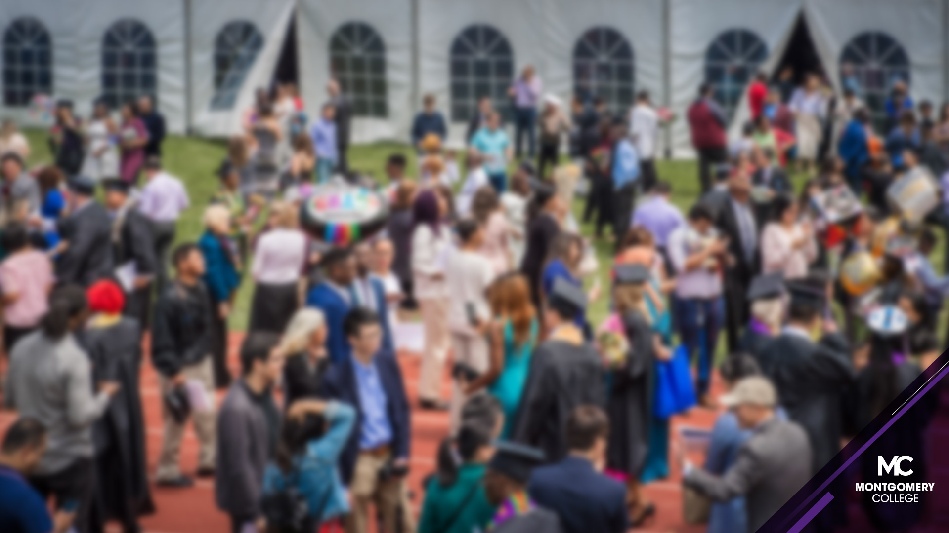 Crowd after commencement outside of the tent mingling. Image has a soft blur.