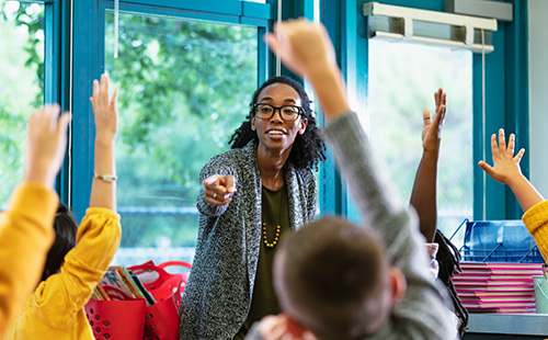Teacher in a classroom with kids raising hands