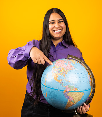 Mariam smiling standing infront of a globe pointing at a specific location